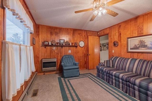 carpeted living room featuring ceiling fan, wooden walls, heating unit, and a textured ceiling