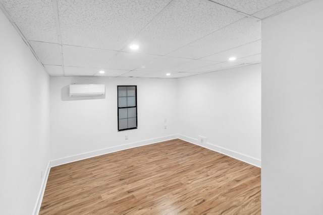 basement with wood-type flooring, an AC wall unit, and a paneled ceiling