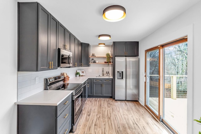 kitchen featuring appliances with stainless steel finishes, tasteful backsplash, sink, gray cabinetry, and light wood-type flooring