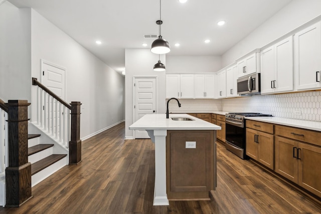 kitchen featuring sink, appliances with stainless steel finishes, white cabinets, a center island with sink, and decorative light fixtures