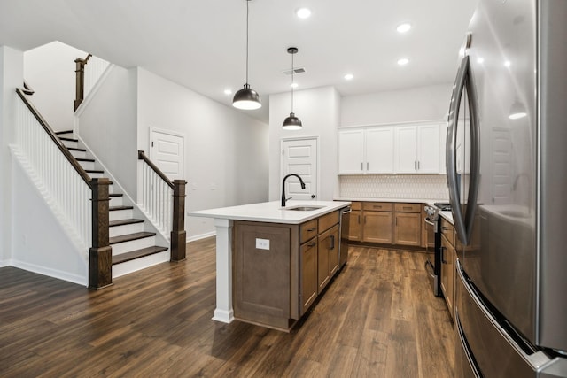 kitchen with sink, appliances with stainless steel finishes, pendant lighting, a kitchen island with sink, and white cabinets