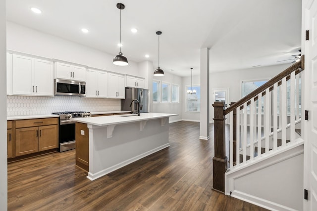 kitchen with appliances with stainless steel finishes, white cabinetry, tasteful backsplash, an island with sink, and decorative light fixtures