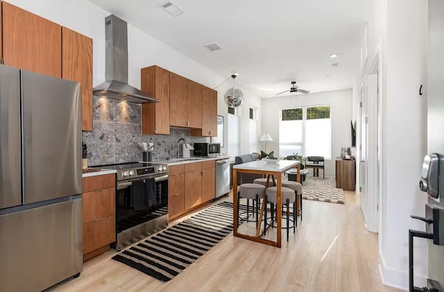 kitchen with backsplash, hanging light fixtures, range hood, stainless steel appliances, and light wood-type flooring