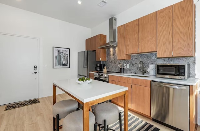 kitchen featuring appliances with stainless steel finishes, sink, decorative backsplash, wall chimney range hood, and light wood-type flooring