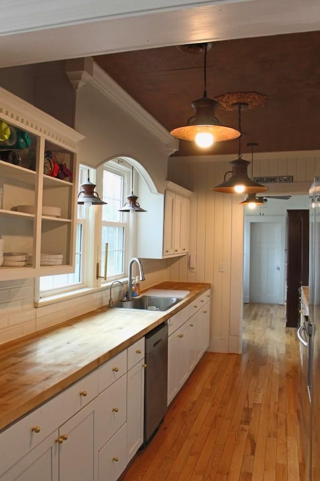 kitchen with wood counters, sink, decorative light fixtures, stainless steel dishwasher, and white cabinets