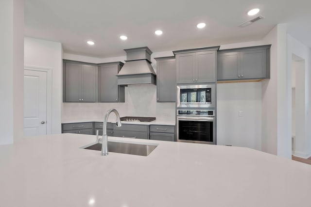 kitchen with custom exhaust hood, appliances with stainless steel finishes, sink, and gray cabinets