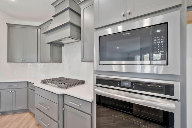 kitchen featuring stainless steel appliances, gray cabinets, custom exhaust hood, and backsplash