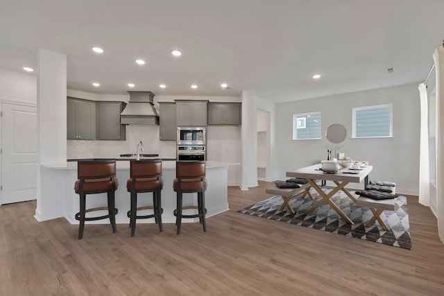 kitchen with gray cabinets, premium range hood, stainless steel appliances, wood-type flooring, and a kitchen bar