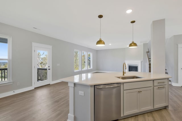 kitchen with sink, dishwasher, a kitchen island with sink, hanging light fixtures, and light wood-type flooring