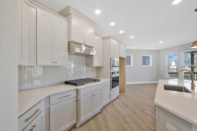 kitchen featuring appliances with stainless steel finishes, sink, white cabinets, decorative backsplash, and light hardwood / wood-style floors