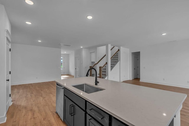 kitchen featuring sink, stainless steel dishwasher, light hardwood / wood-style floors, light stone countertops, and a center island with sink