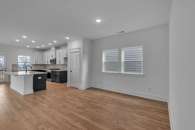 kitchen featuring sink, white cabinetry, a center island with sink, light wood-type flooring, and stainless steel appliances