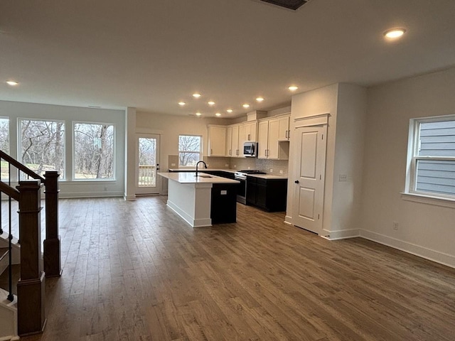 kitchen with dark wood-type flooring, an island with sink, white cabinets, stainless steel appliances, and backsplash