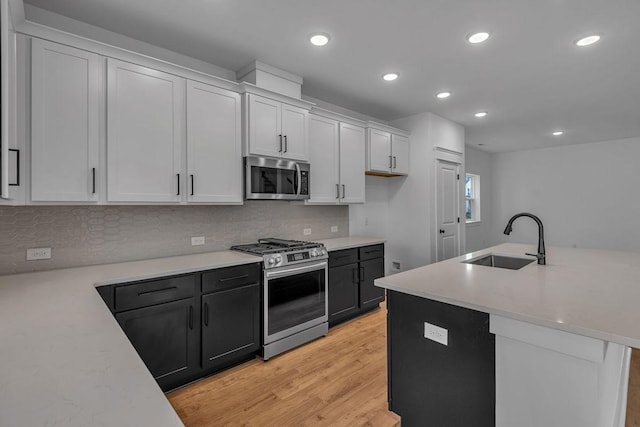 kitchen featuring sink, appliances with stainless steel finishes, light hardwood / wood-style floors, white cabinets, and decorative backsplash