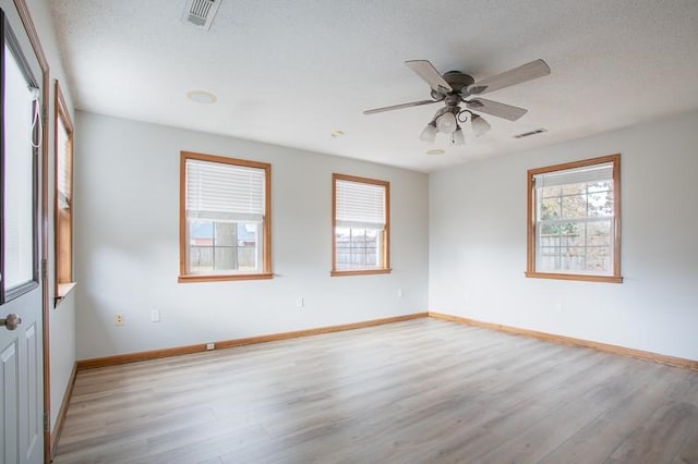 empty room with a wealth of natural light, a textured ceiling, and light hardwood / wood-style flooring