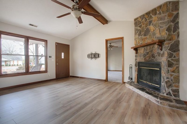 unfurnished living room featuring lofted ceiling with beams, ceiling fan, a stone fireplace, and light hardwood / wood-style floors