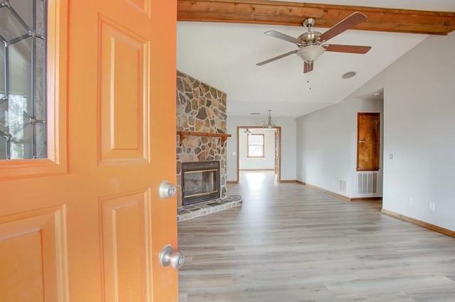 unfurnished living room featuring ceiling fan, a stone fireplace, light hardwood / wood-style floors, and vaulted ceiling with beams