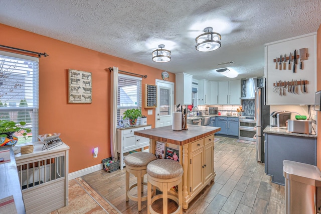 kitchen with wall chimney exhaust hood, a breakfast bar, tasteful backsplash, wooden counters, and white cabinets