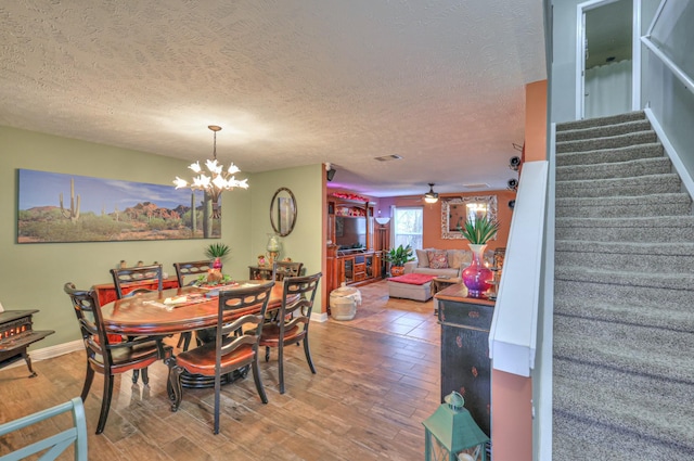 dining area featuring ceiling fan with notable chandelier, wood-type flooring, and a textured ceiling