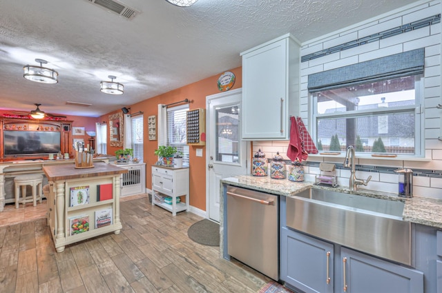 kitchen featuring sink, dishwasher, light stone countertops, white cabinets, and light wood-type flooring