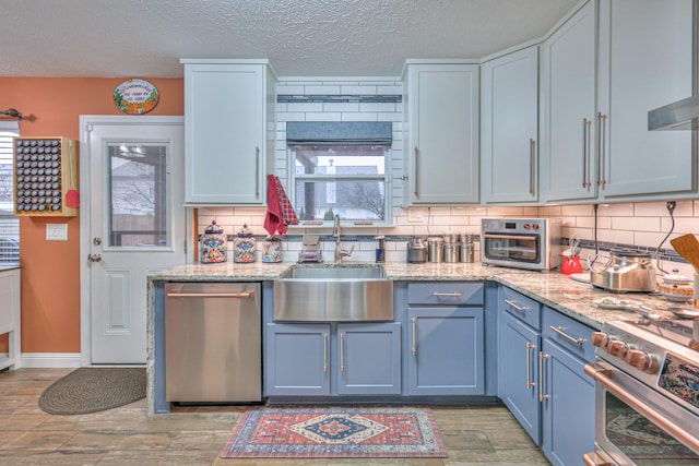 kitchen with appliances with stainless steel finishes, sink, backsplash, light stone counters, and light hardwood / wood-style floors