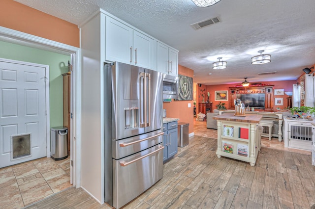 kitchen with a textured ceiling, light hardwood / wood-style floors, white cabinets, and appliances with stainless steel finishes