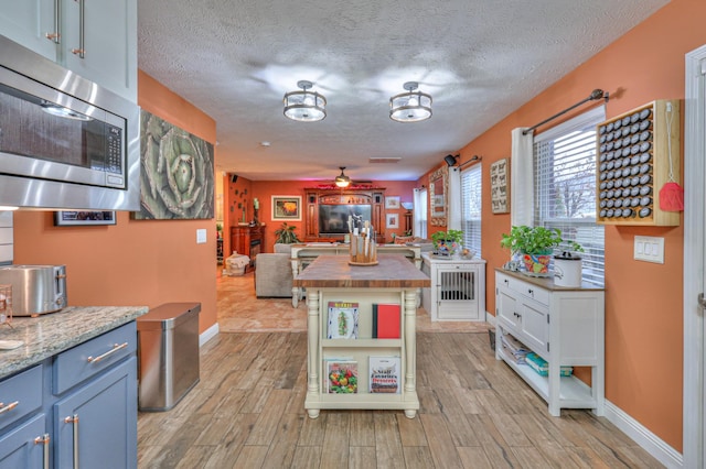 kitchen featuring wood counters, a textured ceiling, stainless steel microwave, ceiling fan, and light hardwood / wood-style floors