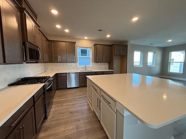 kitchen featuring appliances with stainless steel finishes, sink, backsplash, a center island, and light hardwood / wood-style flooring