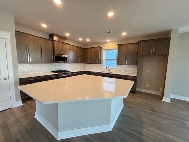 kitchen with sink, dark wood-type flooring, a kitchen island, and appliances with stainless steel finishes