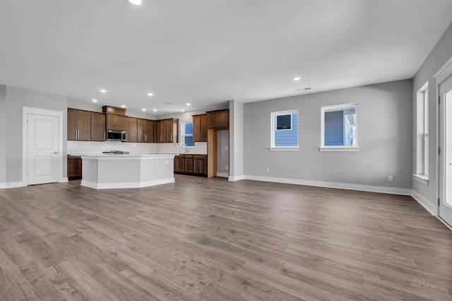 unfurnished living room with a sink, recessed lighting, baseboards, and wood finished floors