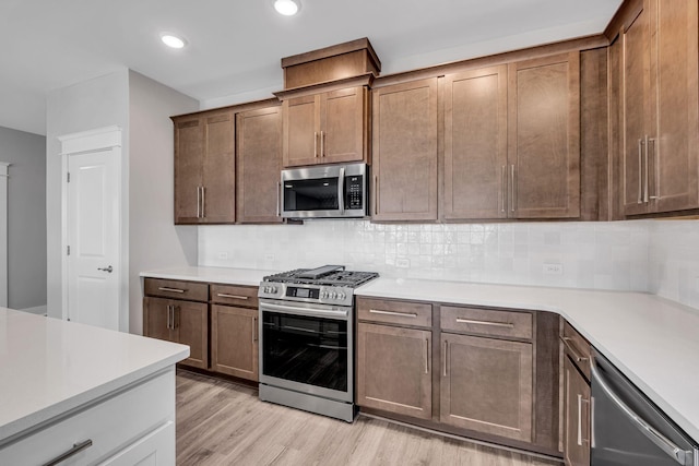 kitchen featuring backsplash, light countertops, light wood finished floors, and appliances with stainless steel finishes