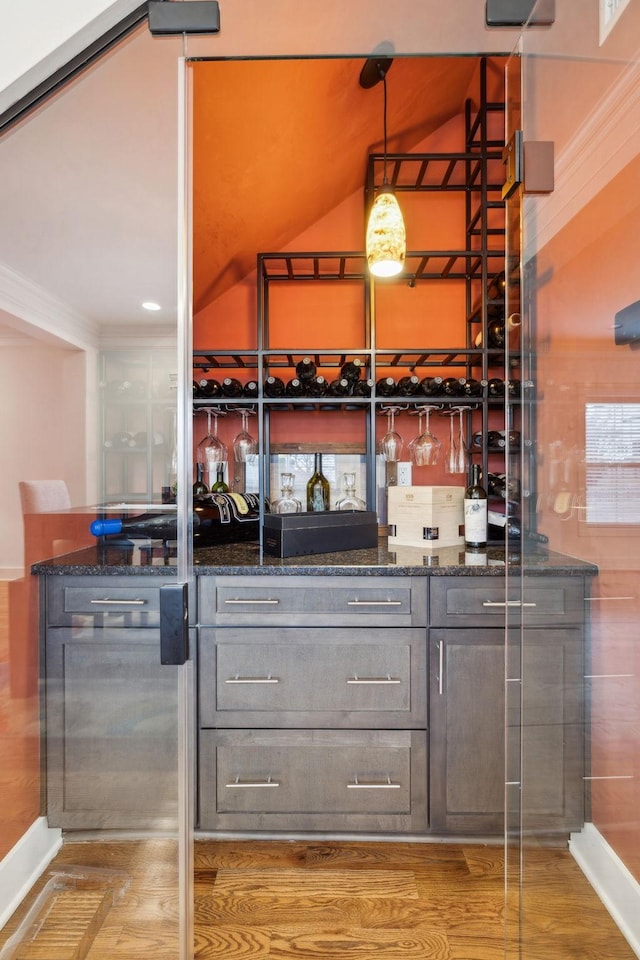 bar featuring dark stone counters, hanging light fixtures, and light wood-type flooring