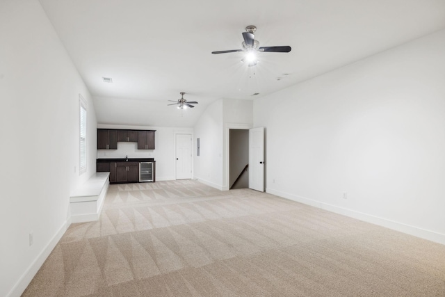 unfurnished living room with vaulted ceiling, light colored carpet, beverage cooler, and ceiling fan