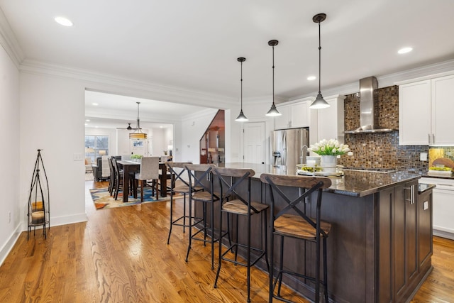 kitchen featuring white cabinetry, stainless steel fridge, hanging light fixtures, a center island, and wall chimney exhaust hood