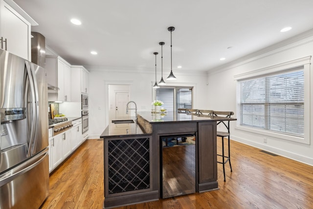 kitchen featuring appliances with stainless steel finishes, an island with sink, white cabinetry, sink, and hanging light fixtures