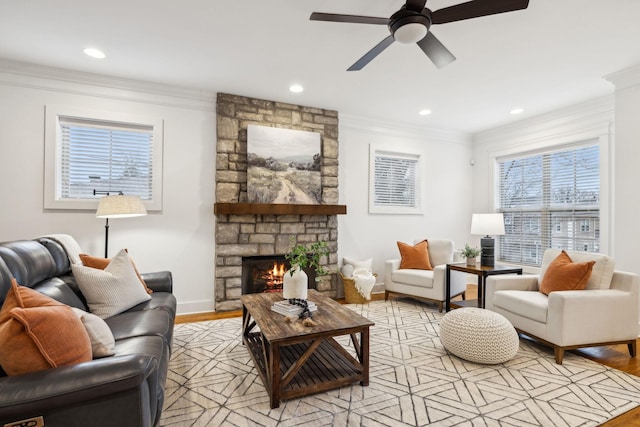 living room featuring crown molding, ceiling fan, a stone fireplace, and light hardwood / wood-style floors