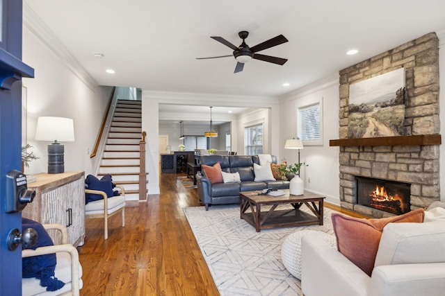 living room with a stone fireplace, wood-type flooring, ornamental molding, and ceiling fan