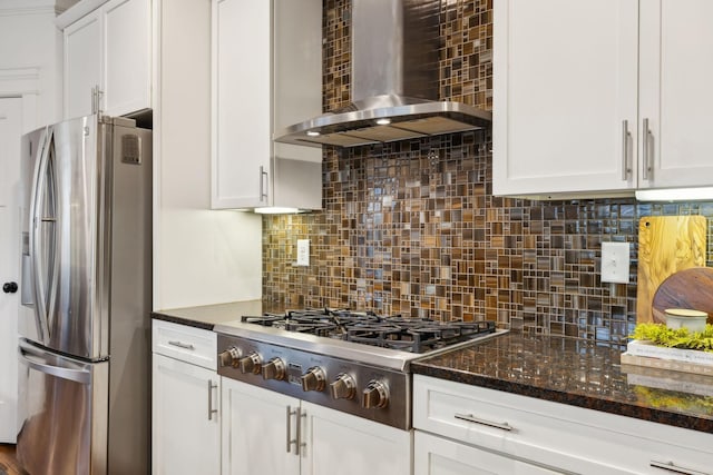 kitchen with tasteful backsplash, dark stone countertops, appliances with stainless steel finishes, wall chimney range hood, and white cabinets