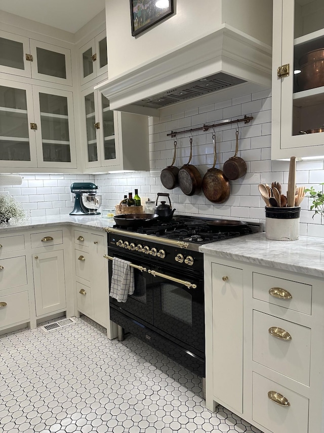 kitchen featuring premium range hood, white cabinetry, double oven range, light stone counters, and tasteful backsplash