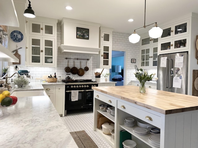 kitchen with wood counters, sink, high end appliances, decorative light fixtures, and white cabinets