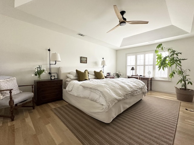 bedroom with hardwood / wood-style floors, a raised ceiling, and ceiling fan