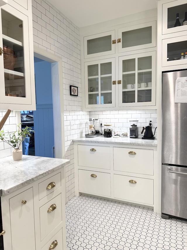 kitchen featuring tasteful backsplash, white cabinetry, light stone counters, and stainless steel refrigerator