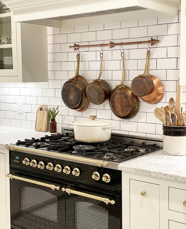 interior details featuring range with two ovens, light stone countertops, white cabinets, and decorative backsplash