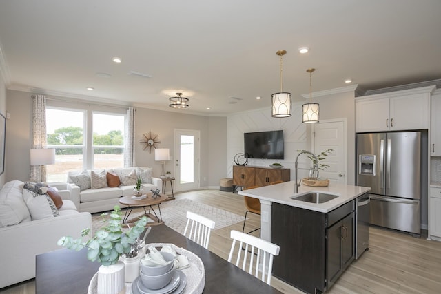 kitchen featuring sink, decorative light fixtures, a center island with sink, stainless steel appliances, and white cabinets