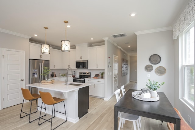 kitchen with pendant lighting, light hardwood / wood-style flooring, a kitchen island with sink, stainless steel appliances, and white cabinets