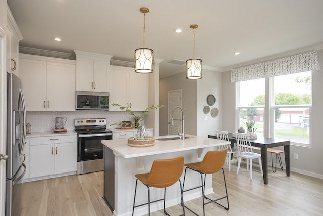 kitchen with a kitchen island with sink, decorative light fixtures, white cabinets, and appliances with stainless steel finishes