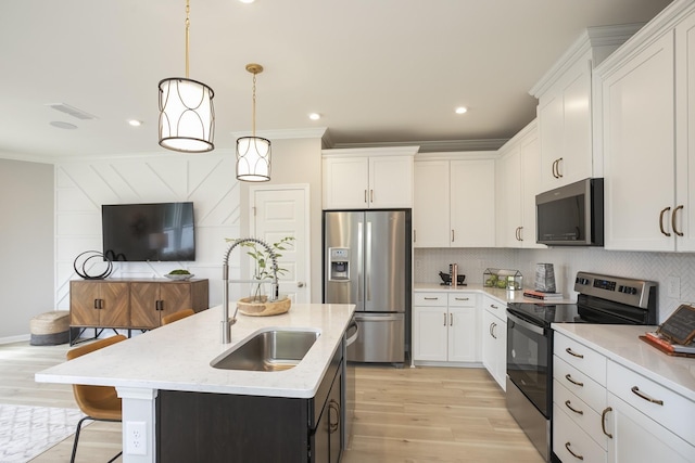 kitchen featuring pendant lighting, sink, white cabinets, stainless steel appliances, and a center island with sink