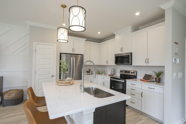 kitchen with sink, hanging light fixtures, stainless steel appliances, white cabinets, and a center island with sink