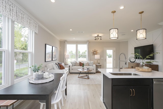 kitchen with pendant lighting, sink, ornamental molding, a center island with sink, and stainless steel dishwasher