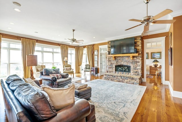 living room with light hardwood / wood-style flooring, crown molding, a stone fireplace, and ceiling fan